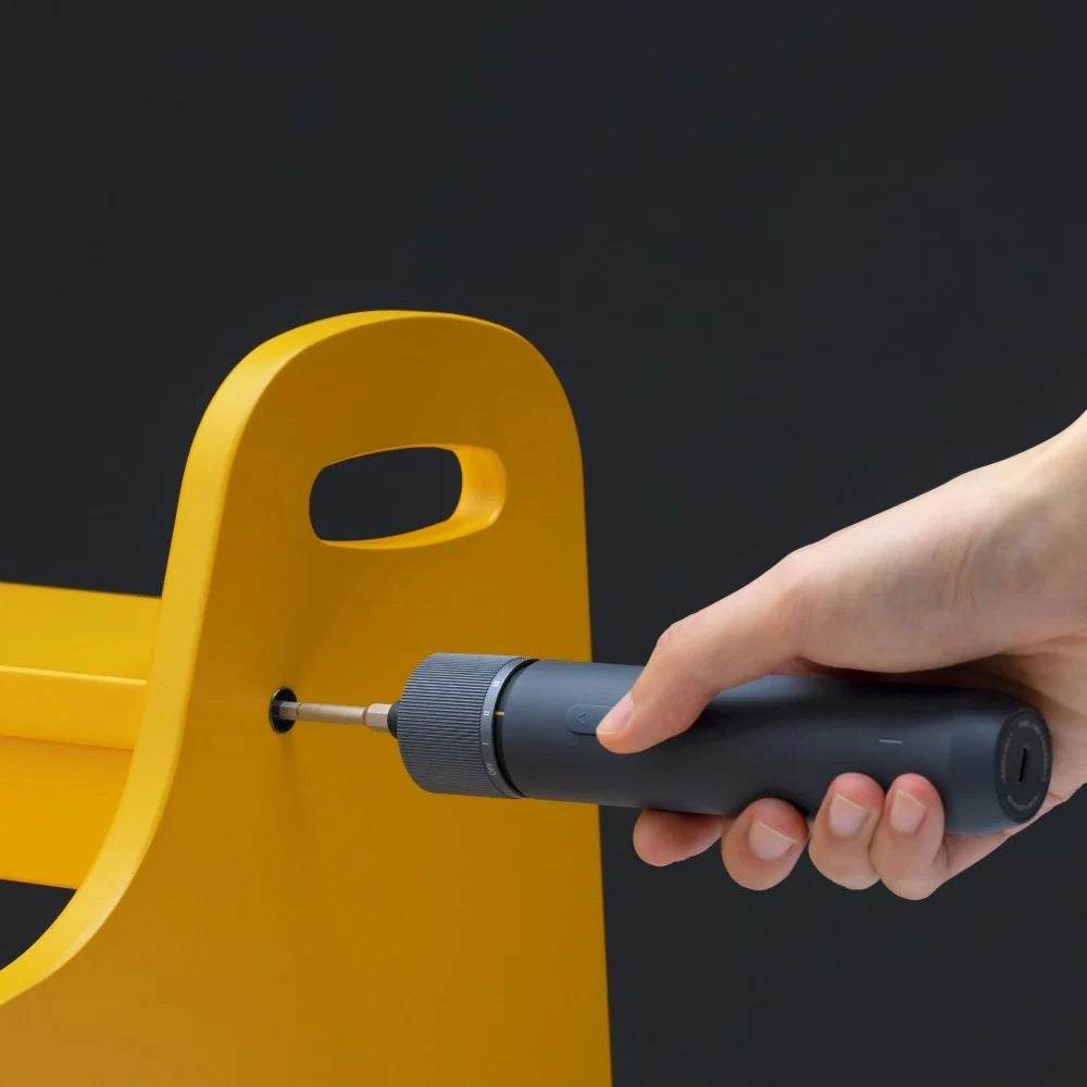 HOTO 3.6V Screwdriver Kit Hand using a black screwdriver on a yellow object against a dark background