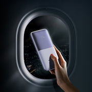 Baseus Bipow Pro Digital Display Fast Charge Power Bank 10000mAh 20W Hand holding a smartphone with a reflective screen in front of an airplane window view.