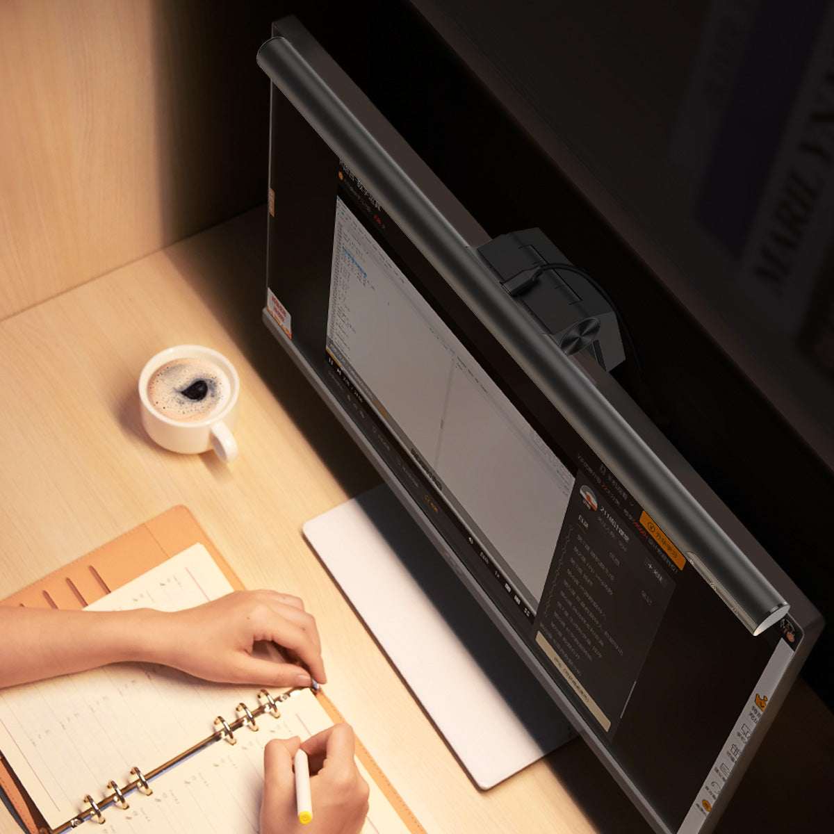Person working at a desk with a computer monitor and notebook.