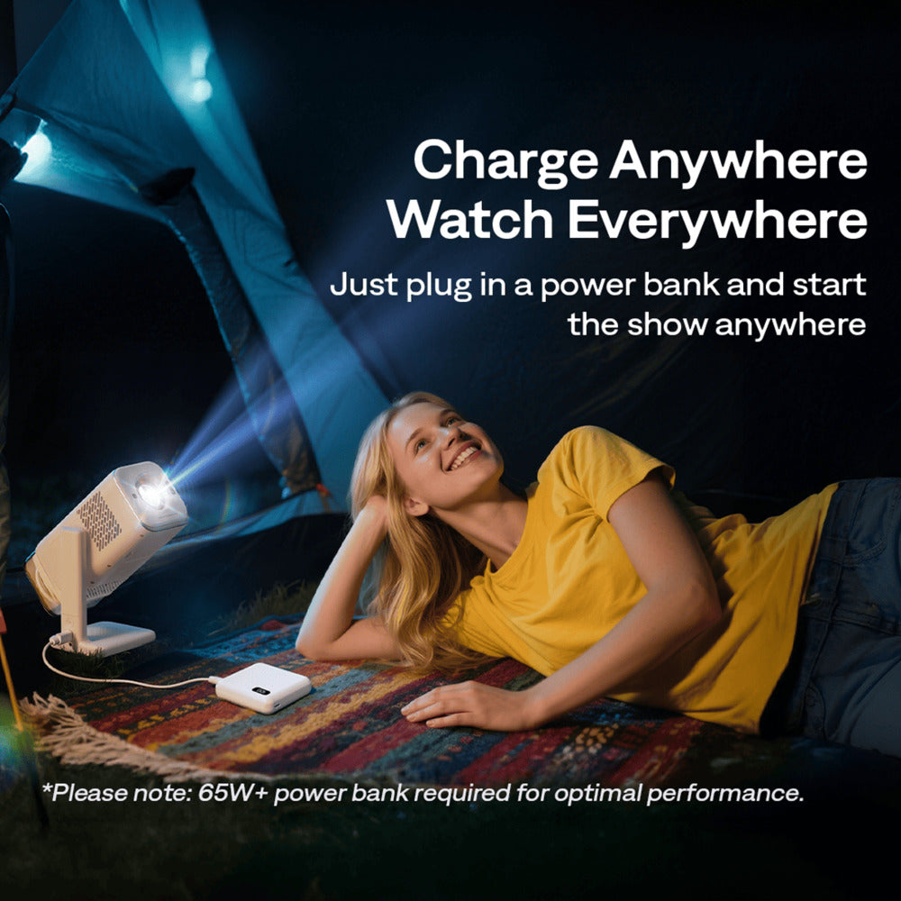 Aurzen Boom Air Portable 1080p Google TV Projector Woman lying on a rug inside a tent with a portable projector and power bank, text 'Charge Anywhere Watch Everywhere'.