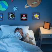 Child sleeping in a bed with a teddy bear, surrounded by wall decorations in a bedroom setting.