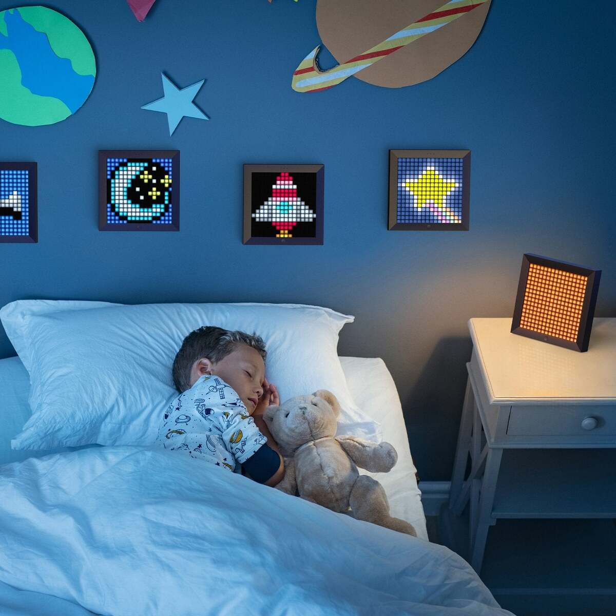 Child sleeping in a bed with a teddy bear, surrounded by wall decorations in a bedroom setting.