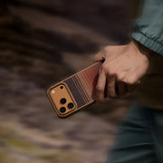 PITAKA ProGaurd Aramid Fibre Case for iPhone 17 Pro Max Person holding a phone with a brown textured case against a blurred natural background