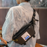 Divoom Pixoo Slingbag‑V Smart LED Sling Bag (4.7" Pixel Screen, App Control) Person wearing a black crossbody bag with a digital display, standing indoors.
