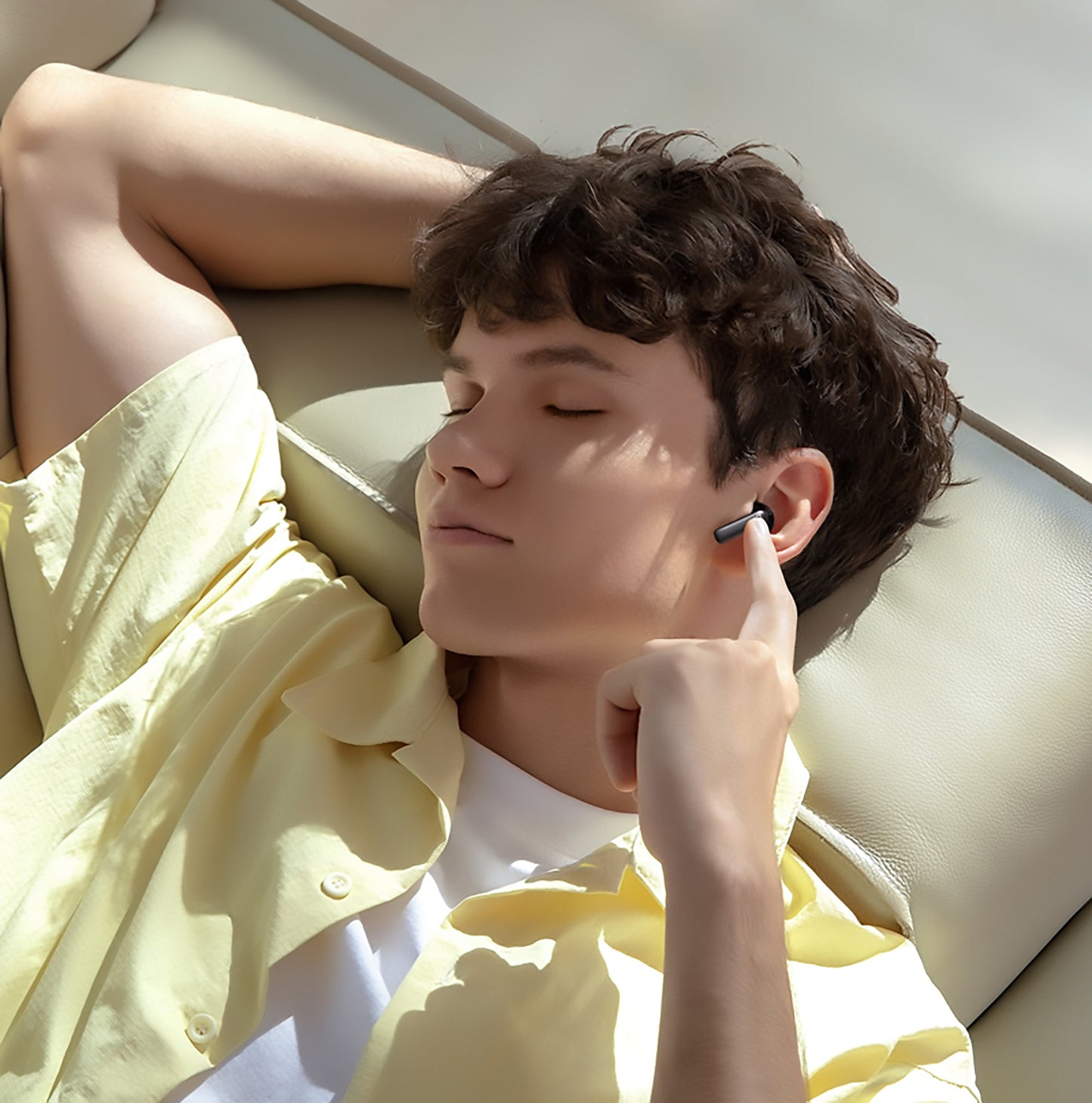 Person wearing wireless earbuds, lying on a couch in a bright room