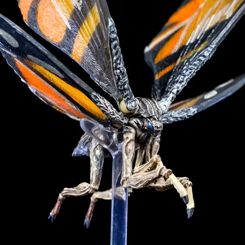 Metallic butterfly figurine with orange, black, and yellow wings on a clear stand against a black background