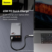 Baseus 65W PD quick charge device charging a laptop on a wooden surface.