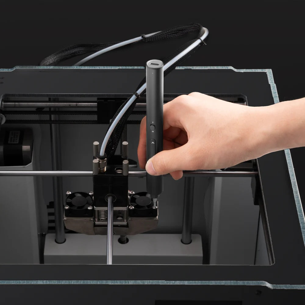 Hand holding a pen-like device near a 3D printer on a black background