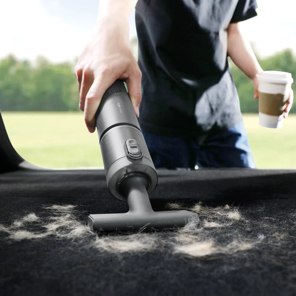 Person using a handheld vacuum cleaner on a car roof with a blurred outdoor background