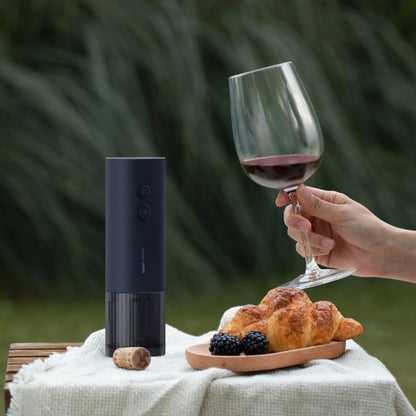 HOTO Electric Wine Opener .Wine bottle opener, glass of red wine, and croissants on a table outdoors.
