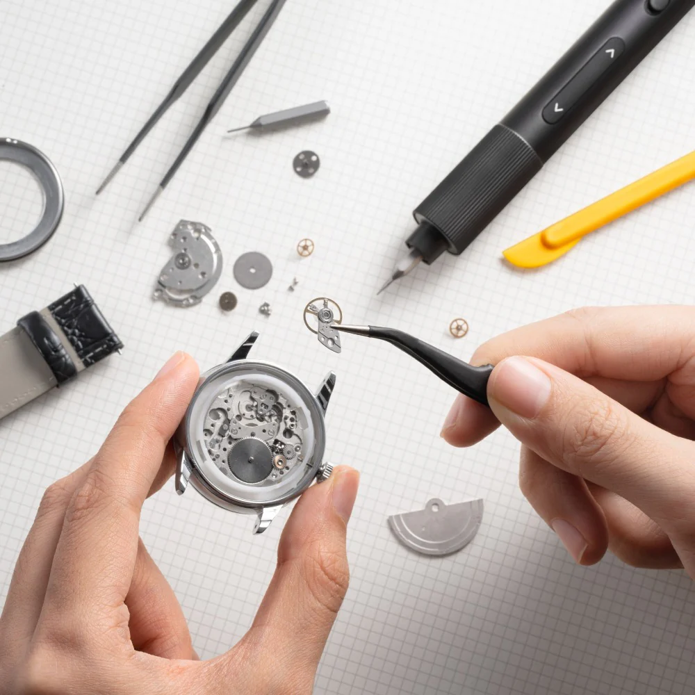 Watch repair process with hands using tools on a white surface