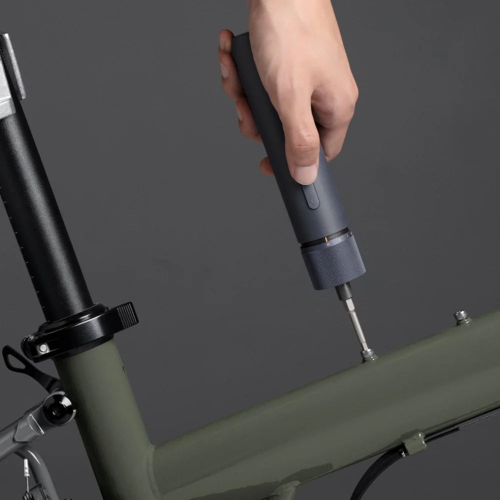 HOTO 3.6V Screwdriver Kit, Hand using a tool on a bicycle frame against a dark background