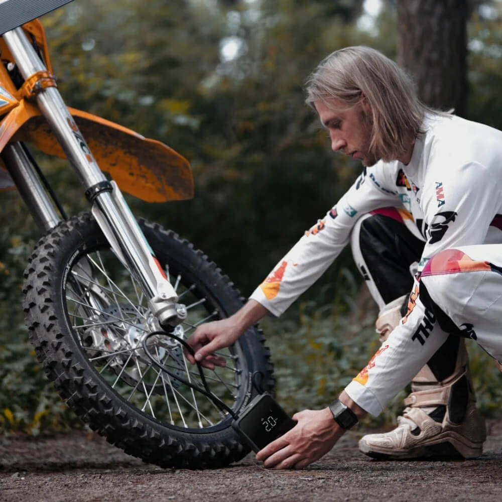 HOTO Air Pump Pro Portable Tire Inflator 120 PSI Person adjusting a tire on a dirt bike with a digital display in an outdoor setting