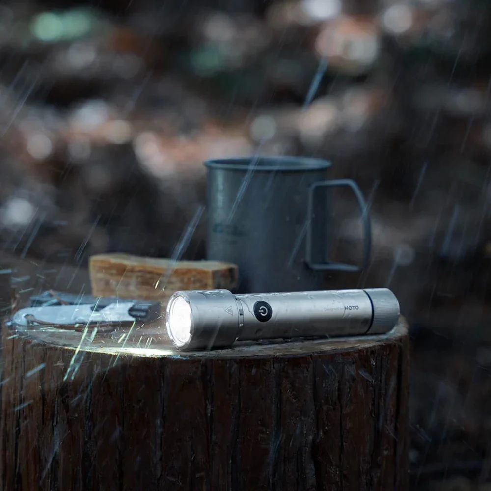 HOTO Flashlight Tactics 2300 Tactical Rechargeable Torch Flashlight on a log with a blurred background of a campfire and mug