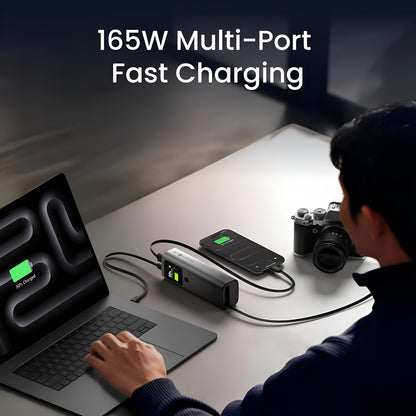 Sharge Retractable 165W Power Bank (20000mAh, Built‑in 100W USB‑C Cable) Person using a 165W multi-port charging station with laptop, phone, and camera on a desk.