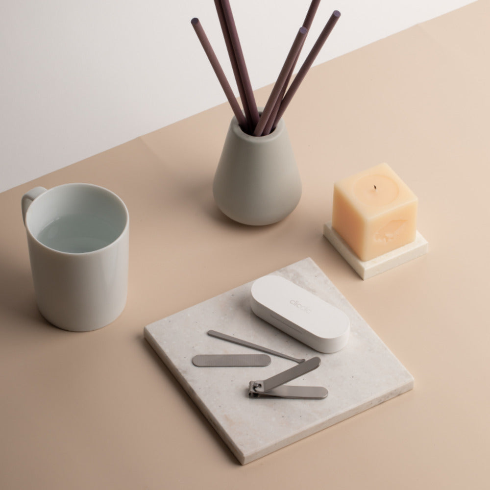 HOTO Clicclic Three-piece Nail Clipper, Ceramic mug, diffuser, and candle on a beige surface