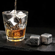 Glass of whiskey with ice cubes and metal stones on a dark surface