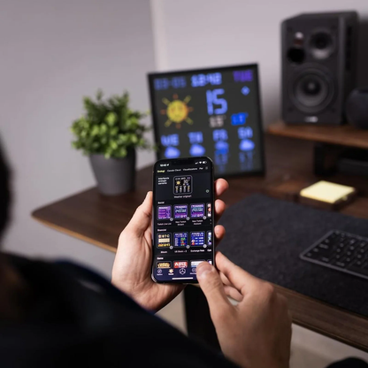 Divoom Pixoo 16×16 RGB Pixel LED Display (Smart App, Desktop & Wall Mount) Person holding a smartphone with a weather app in front of a computer screen displaying the same weather information.
