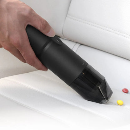 HOTO Compressed Air Capsule, Hand using a black handheld vacuum cleaner on a car seat.
