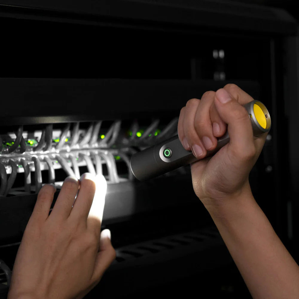 Person using a flashlight to inspect network equipment in a server room.