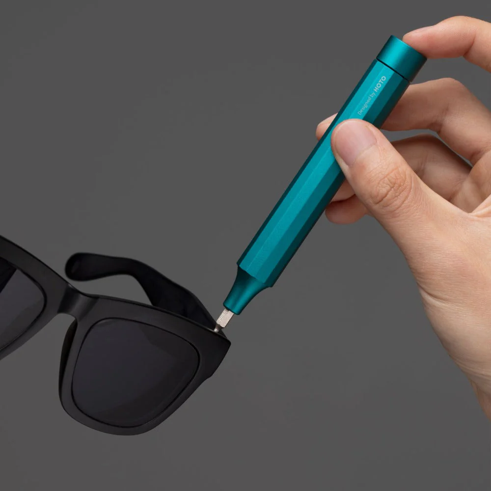 Hand holding a blue tool near a pair of black sunglasses on a dark background
