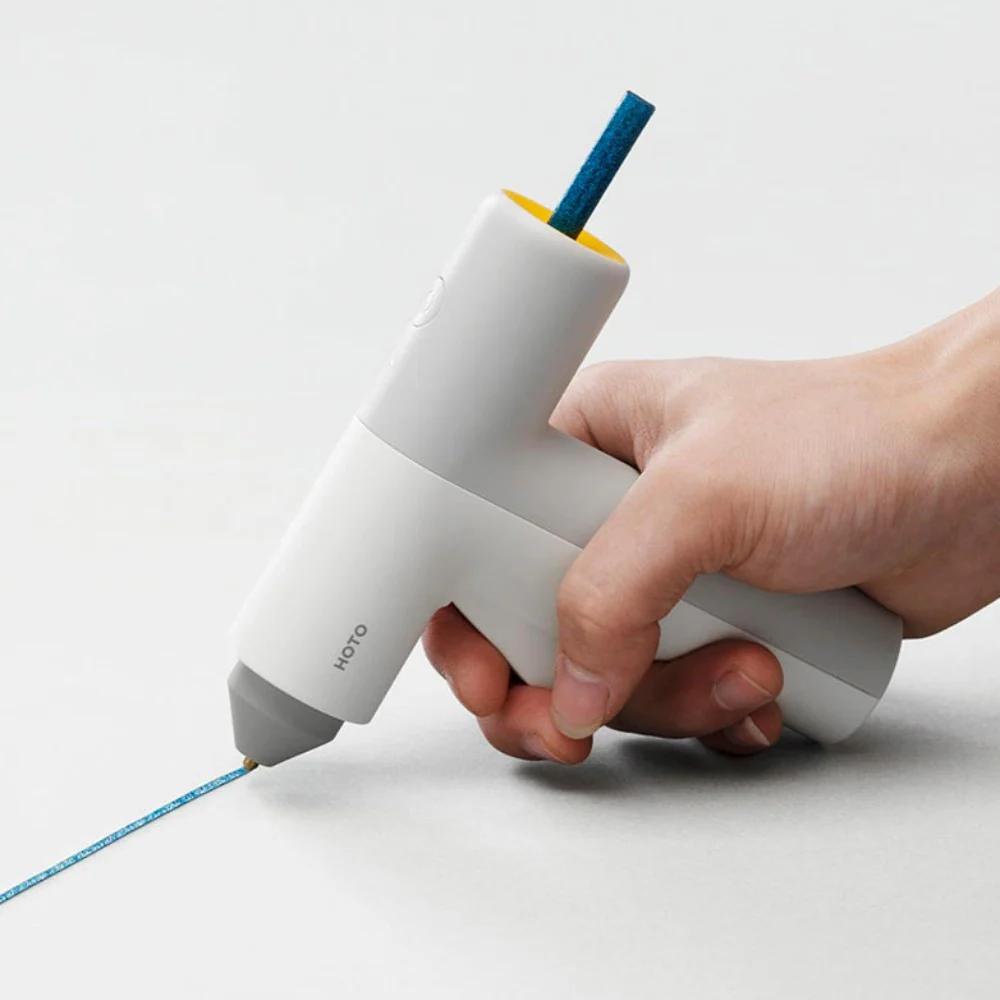 HOTO Hot Melt Glue Sticks, Hand holding a white hot glue gun with blue glue being applied on a light gray background