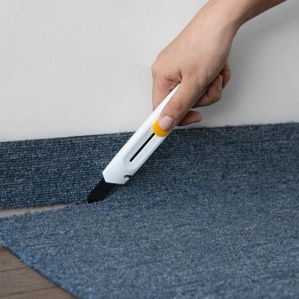 Hand using a carpet edge trimmer on a blue carpet