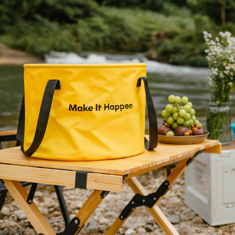 HOTO Outdoor Wash Kit, Yellow cooler bag with 'Make It Happen' text on a wooden table by a river.