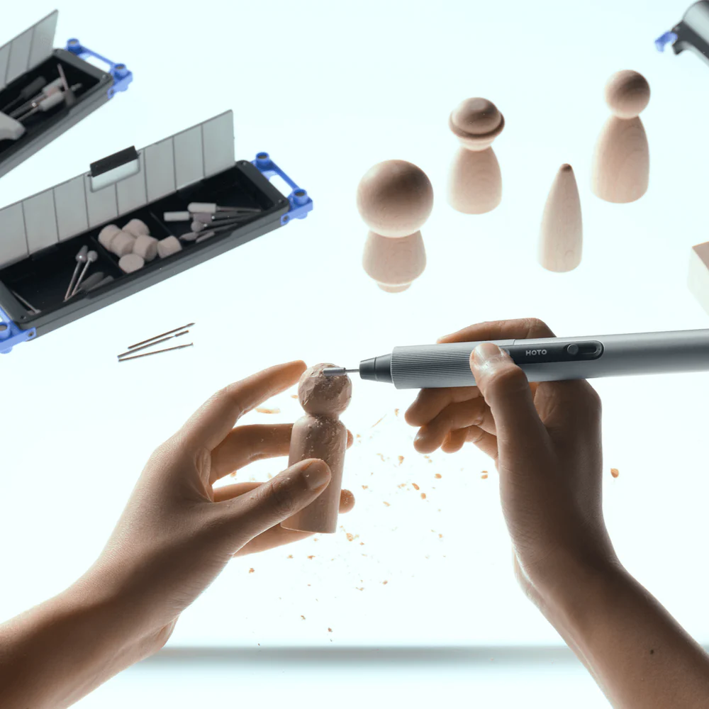 Hands using a tool to work on small wooden figures with a white background.