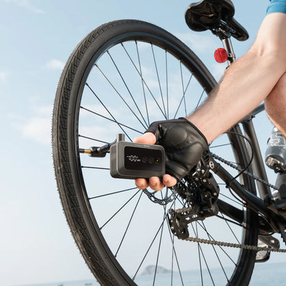HOTO Air Pump Pocket, Person using a digital bike pump to inflate a bicycle tire outdoors.