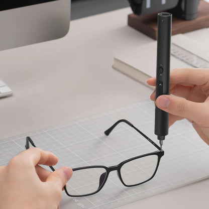 Person using a black pen-like device on a pair of glasses on a desk.