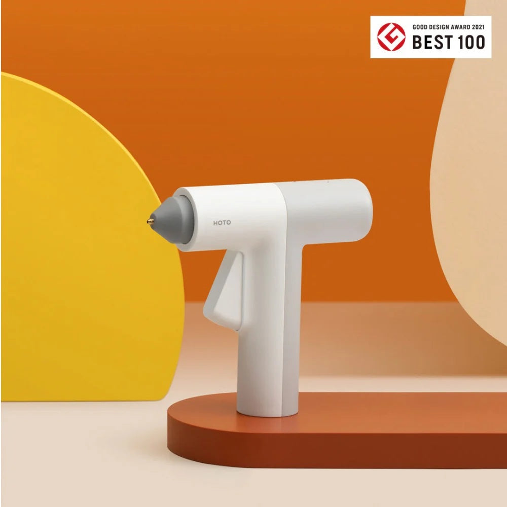 HOTO Lithium Glue Gun, White handheld device with gray nozzle on an orange and yellow background, featuring the Good Design Award 2021 Best 100 logo.