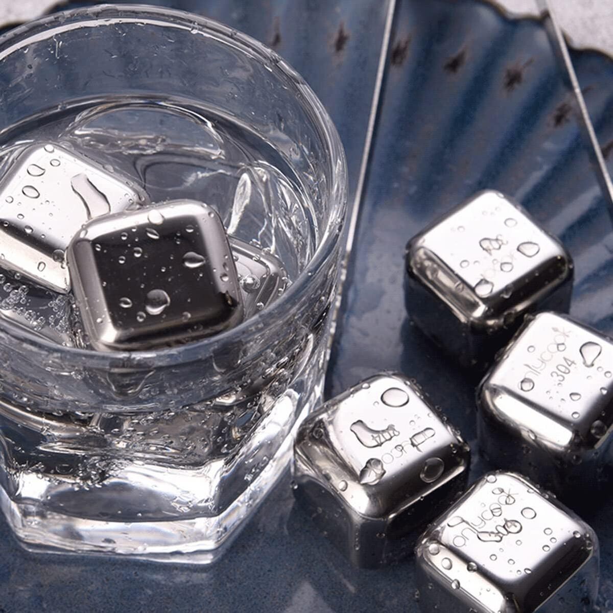 Metallic ice cubes in a glass of water on a reflective surface