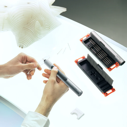 Person holding a pen with a transparent cartridge, surrounded by additional cartridges and a small model.