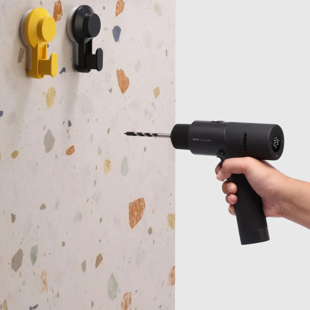 Hand holding a drill against a textured wall with hooks attached.