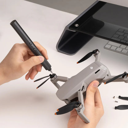 Person assembling a drone with a tool on a desk.