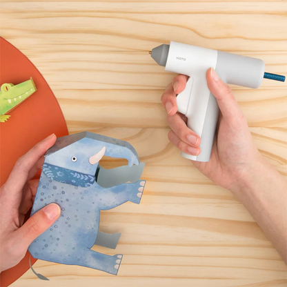 HOTO Hot Melt Glue Sticks, Hand holding a paper craft of a blue dinosaur with a hot glue gun on a wooden surface