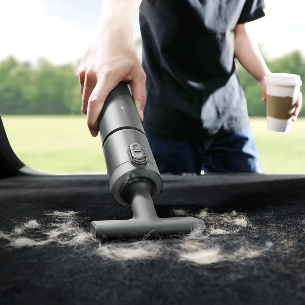 Person using a handheld vacuum cleaner on a car roof with a blurred outdoor background