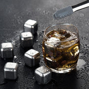 Glass of whiskey with metal ice cubes and tongs on a dark surface