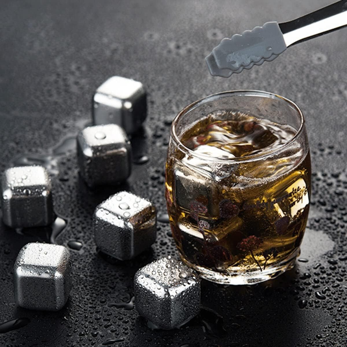 Glass of whiskey with metal ice cubes and tongs on a dark surface