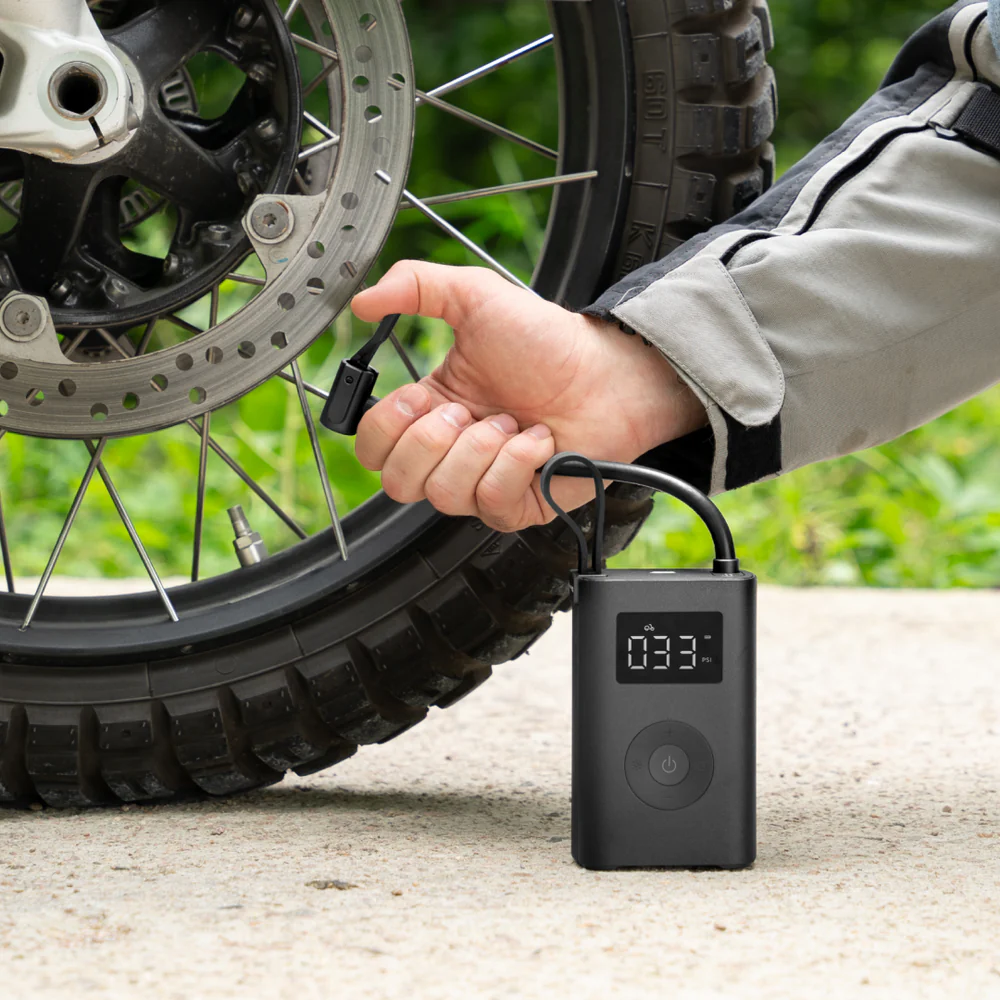 HOTO Electric Air Pump, Person using a digital tire pressure gauge on a motorcycle tire outdoors.