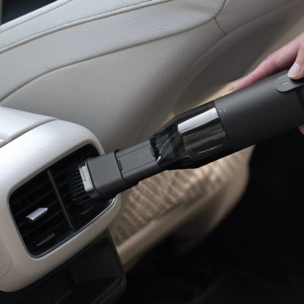 Hand using a handheld vacuum cleaner to clean inside a car.