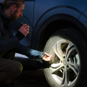 HOTO Flashlight Tactics 2300 Tactical Rechargeable Torch Person inspecting a car tire with a flashlight at night.