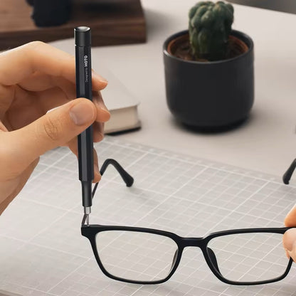 HOTO Pocket Precision Screwdriver SE Hand holding a pen near eyeglasses on a desk with a cactus in the background