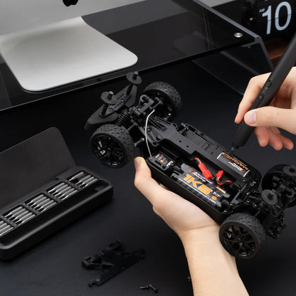 Person assembling a black RC car with tools on a dark surface