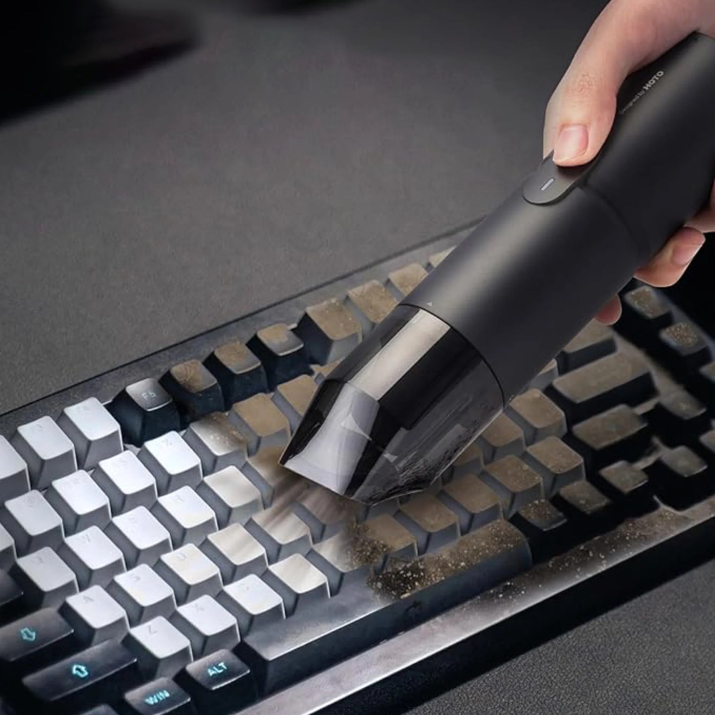 Person cleaning a keyboard with a handheld vacuum cleaner.