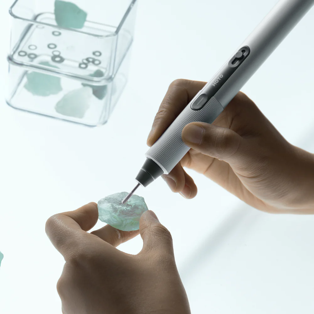 Person using a small tool on a piece of jewelry with a clear container of additional parts in the background.