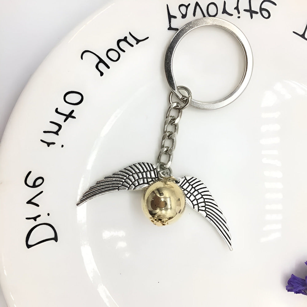Keychain with a gold sphere and silver wings on a white plate with text / Harry Potter Golden Snitch Keyring