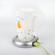 USB Mug Warmer And 4 Port Hub, White mug with a cat illustration on a silver mug warmer plugged into a white wall outlet.