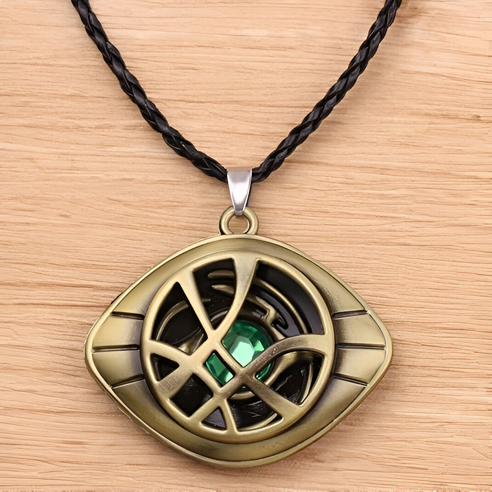 Bronze pendant with green gemstone on a black cord against a wooden / Marvels Doctor Strange - Eye of Agamotto Necklace background